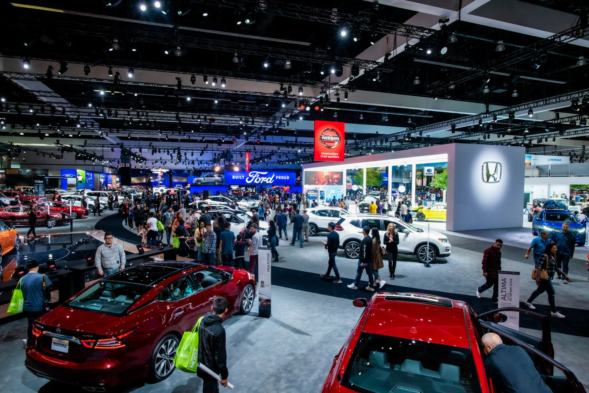 Crowded auto show showcasing various car brands like Ford, Nissan, and Honda, highlighting vehicles and automotive innovations